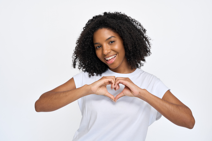 Happy young African woman showing heart sign isolated at white wall background.