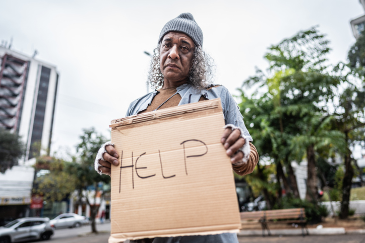 Portrait of a senior homeless man with a cardboard sign asking for help at the public park
