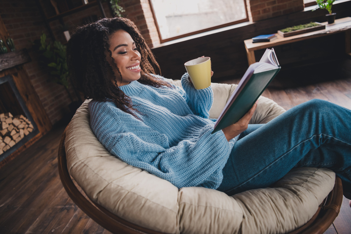 Young woman enjoying a cozy autumn day indoors while reading and sipping coffee from a mug