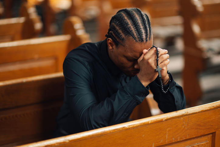 Young man praying with rosary in church pew