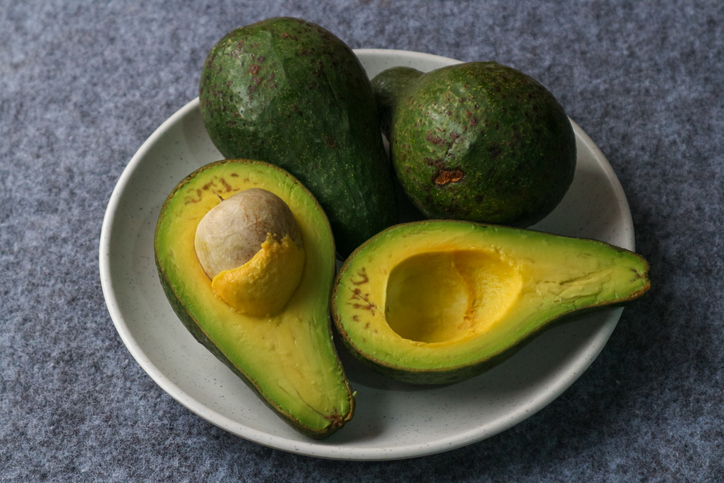 Organic avocados half cut with seed and whole fruit in plate