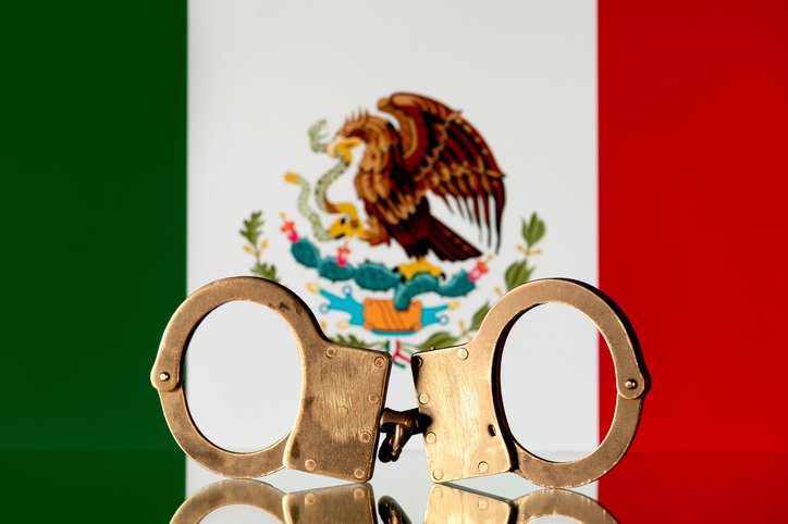 Steel handcuffs on the background of the flag of Mexico
