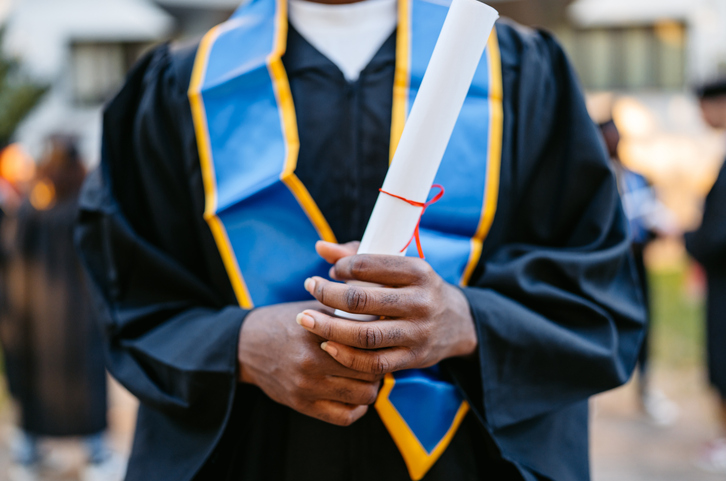 Young Male Student In Graduation Gown Standing On The University Campus