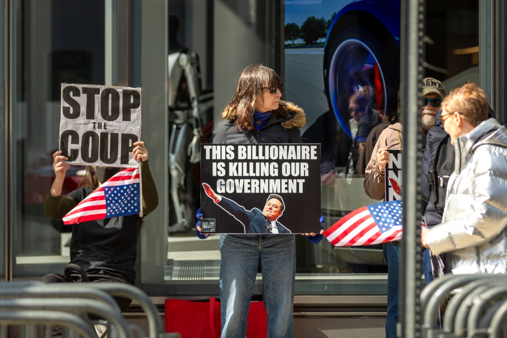 A protester holds signs that read: "This billionaire is...