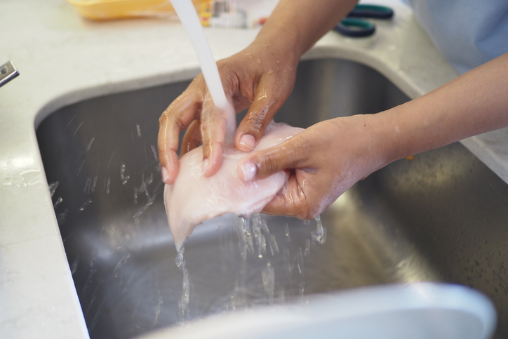 Female hands washing and cleaning chicken breast .