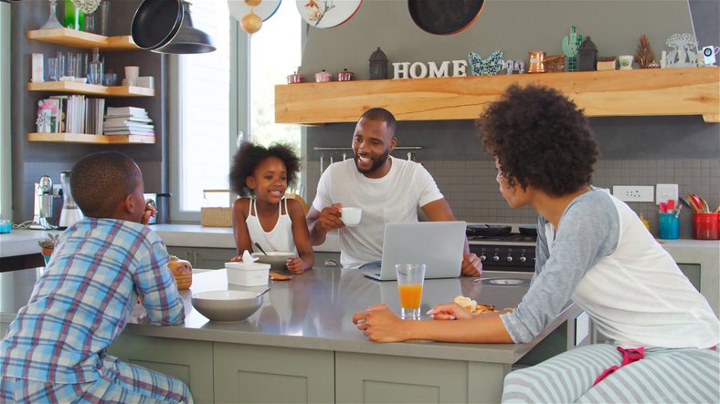 Family Wearing Pyjamas Sitting In Kitchen Enjoying Morning Breakfast Together