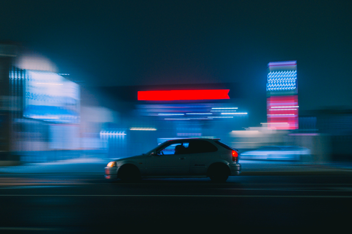Racing car passing by illuminated gas station at night