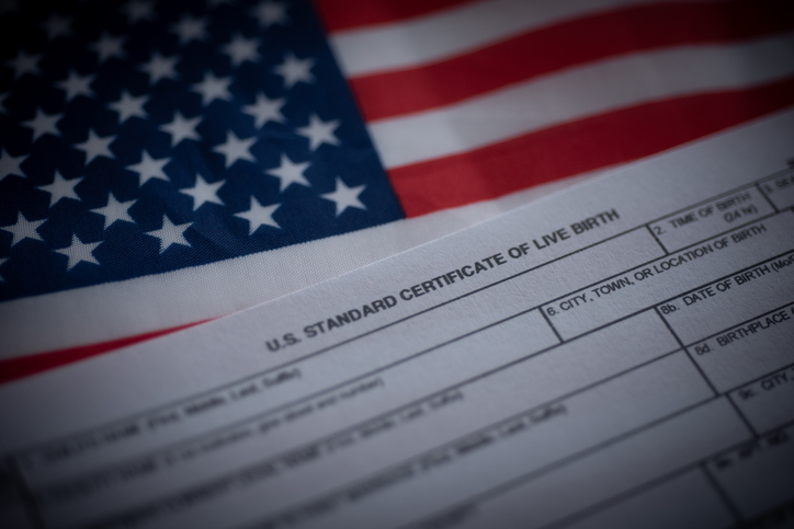 U.S. standard certificate of live birth application form next to flag of USA. Birthright citizenship concept.