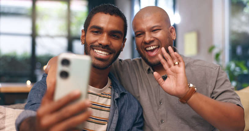 Gay, love and happy couple on video call in home together for bonding, relationship or communication. Virtual chat, lgbtq or men with smile or greeting on mobile app for social media, wave or selfie