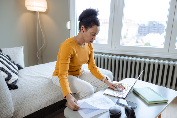Woman working at home on laptop with documents