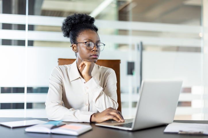 Serious thinking woman at workplace inside office, businesswoman preparing electronic presentation on laptop, office worker reading financial report online from computer screen