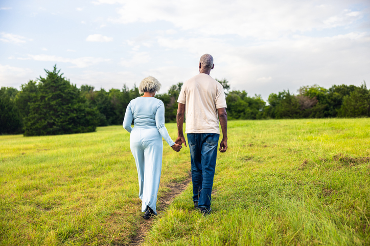 Beautiful senior black couple walking in a green pasture with trees