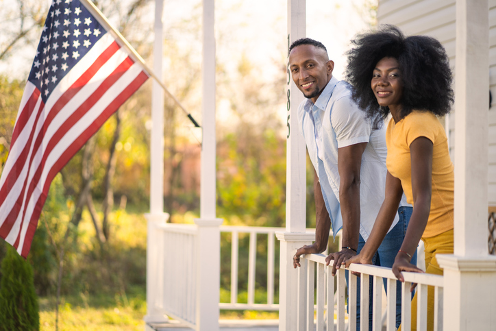 A young couple leaning on a front porch with American flag