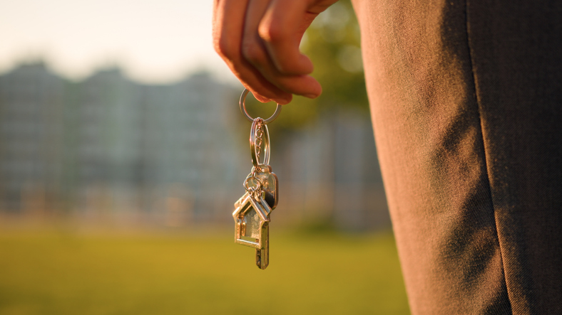 Cropped view female hand African American woman girl real estate agent buyer holding bunch of keys to new house own flat home ownership real estate in city park lawn background of blurred skyscrapers buildings