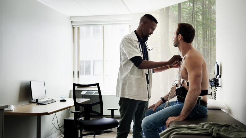 Doctor attaching electrodes to patient during electrocardiogram in clinic room - Young Doctors Project