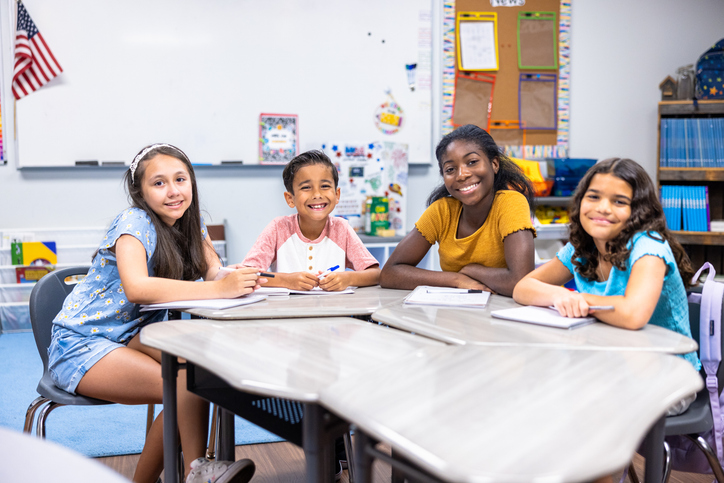 Group of schoolchildren at the desk smiling at the camera
