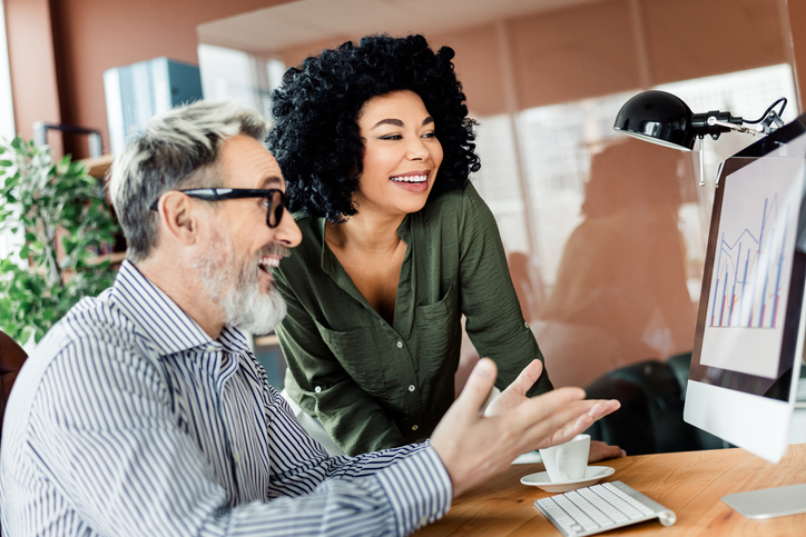 Professional coworkers engaged in teamwork discussion in a corporate office environment, analyzing data on a computer screen